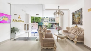 Un hall d’hôtel moderne avec une entrée en verre, un lustre et un ensemble de canapés.