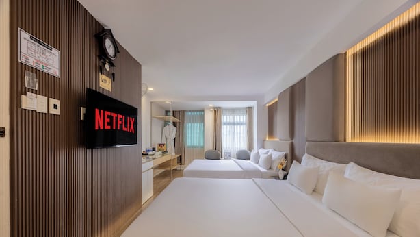 Une chambre d’hôtel avec deux lits, un écran de télévision affichant le logo « NETFLIX », une horloge et une pancarte indiquant « VIP 7 ».