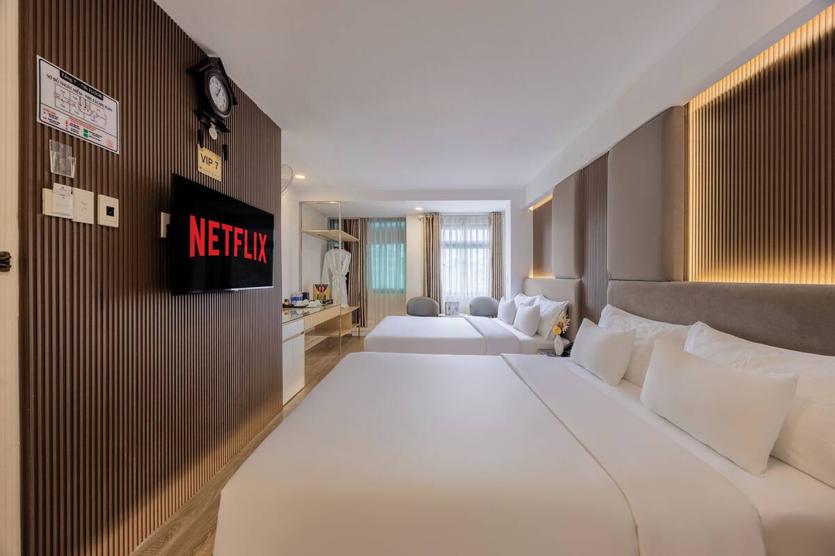 A hotel room with two beds, a TV screen displaying 'NETFLIX', a clock, and a 'VIP 7' sign.
