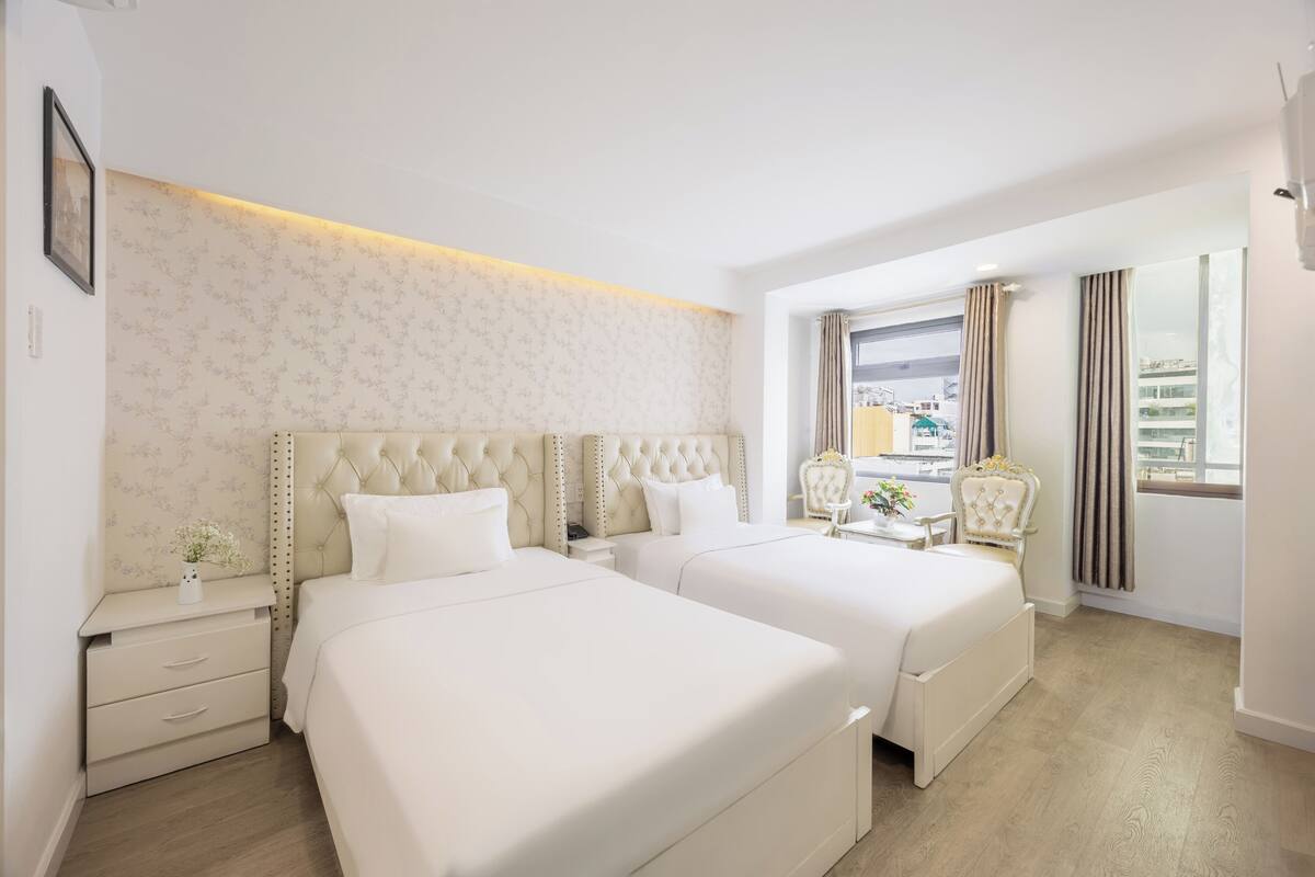 A hotel room with two beds, a nightstand, a dresser, and a window with curtains.