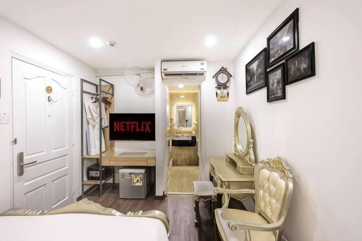 A hotel room with a bed, a vanity with a mirror, a chair, a desk, a television, and a wardrobe.