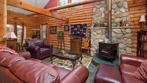A log cabin interior with leather sofas, a stone fireplace, and a guitar. - Beautiful Log Cabin | Wooded | Lake Access | Interlochen Arts Academy (Interlochen)