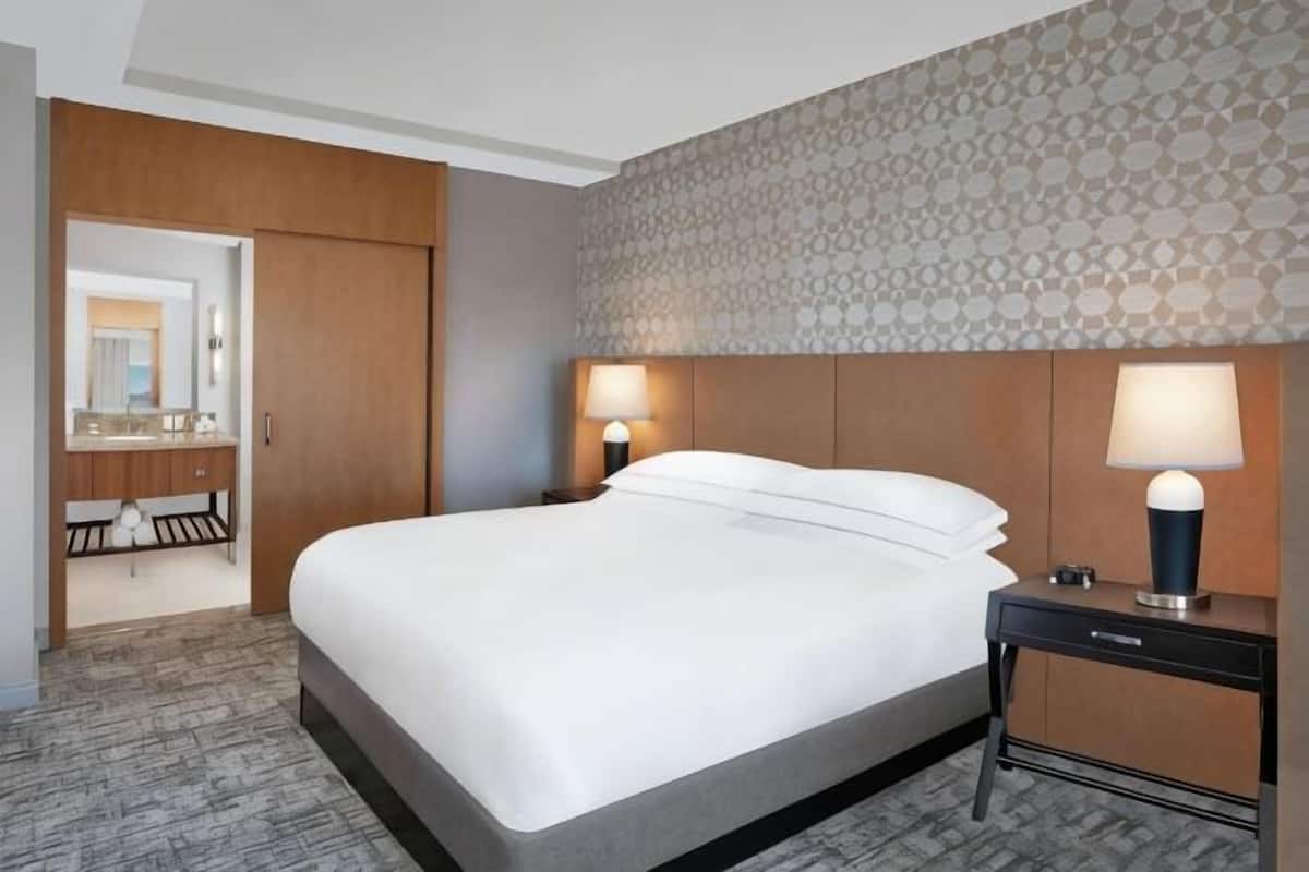 Ein Hotelzimmer mit einem großen Bett, Nachttischlampen, einem Schreibtisch und einem Spiegel.
