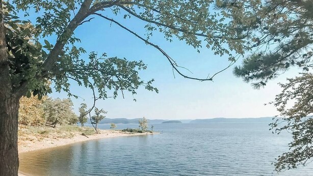 A lakeside view with a sandy beach and trees. - 2-Cabin Retreat| Pool Table | Hot Tubs | Mini Golf (Broken Bow)