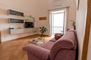 A living room with a sofa, a coffee table, a TV, and a balcony with a plant.