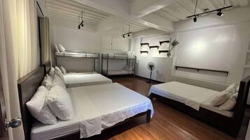 Habitación de hotel con dos camas individuales, una litera y suelo de madera, además de un ventilador de techo.