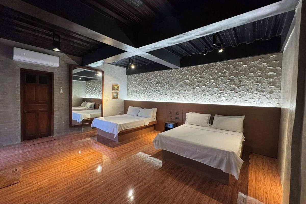 Een hotelkamer met twee bedden, een houten vloer, een structuurwand en een plafond met zichtbare balken.