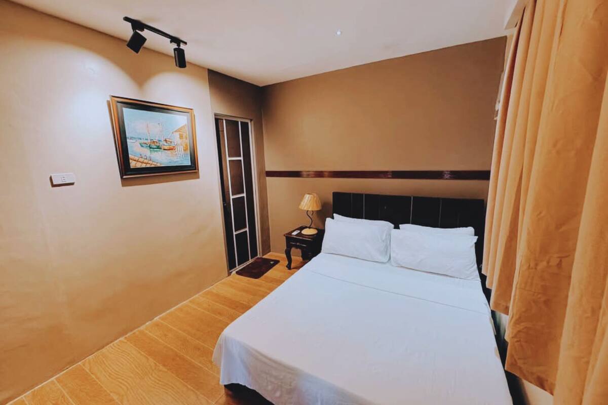 Een hotelkamer met een bed, nachtkastje, lamp, schilderij aan de muur en een deur.