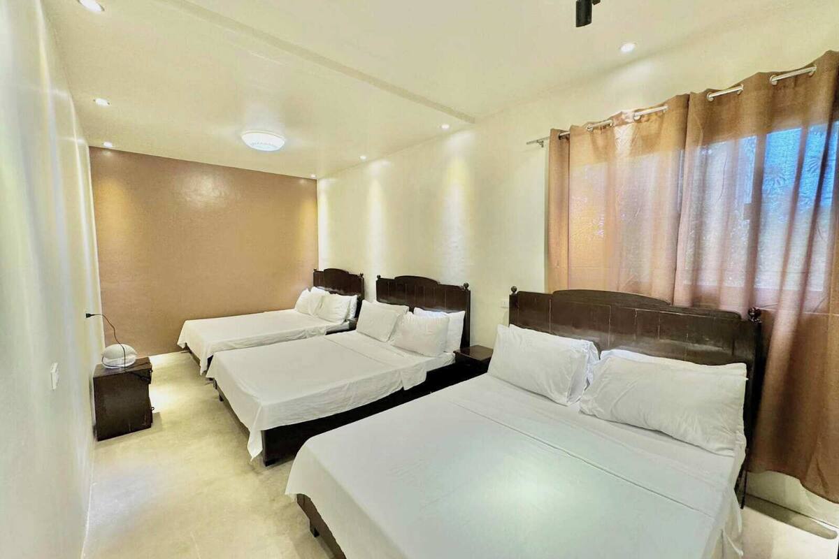 Een hotelkamer met drie eenpersoonsbedden, een nachtkastje en een raam met gordijnen.