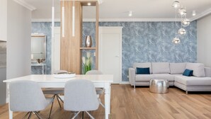 Ein modernes Wohnzimmer mit einem weißen Sofa, grauen Sesseln, einem Holztisch und einem Essbereich mit Tisch und Stühlen in Weiß.