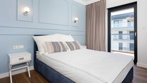 Ein Schlafzimmer mit Bett, Nachttisch, Wandleuchten und Blick auf einen Balkon.