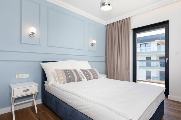 A bedroom with a bed, nightstand, wall sconces, and a view of a balcony.