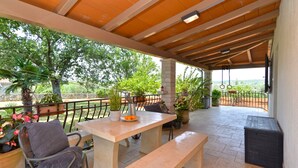A covered outdoor seating area with a table and benches, surrounded by potted plants and a view of trees and hills. - House 2174/55597 (Istria - Rovinj), 600m from the beach (Rovinj)