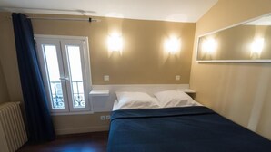 A bedroom with a bed, a window with curtains, a radiator, and wall-mounted lights. - Hôtel De La Gare (Villeneuve-Saint-Georges)