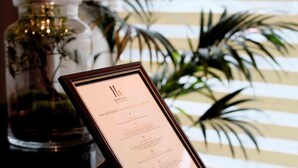 A framed welcome sign with text, a glass jar with greenery, and a striped wall with plants in the background. - Hôtel De La Gare (Villeneuve-Saint-Georges)
