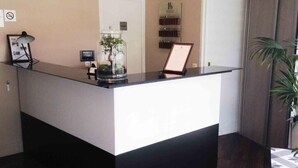 A reception desk with a glass enclosure containing a plant, a framed picture, and a small table with a lamp. - Hôtel De La Gare (Villeneuve-Saint-Georges)