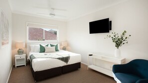 Quarto com cama, mesas de cabeceira, televisão, planta e uma cadeira.