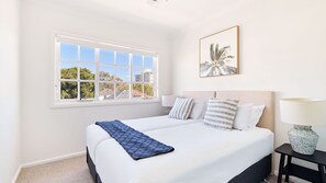 Une chambre d’hôtel avec un grand lit, une table de chevet, une lampe et une fenêtre donnant sur des immeubles et des arbres.