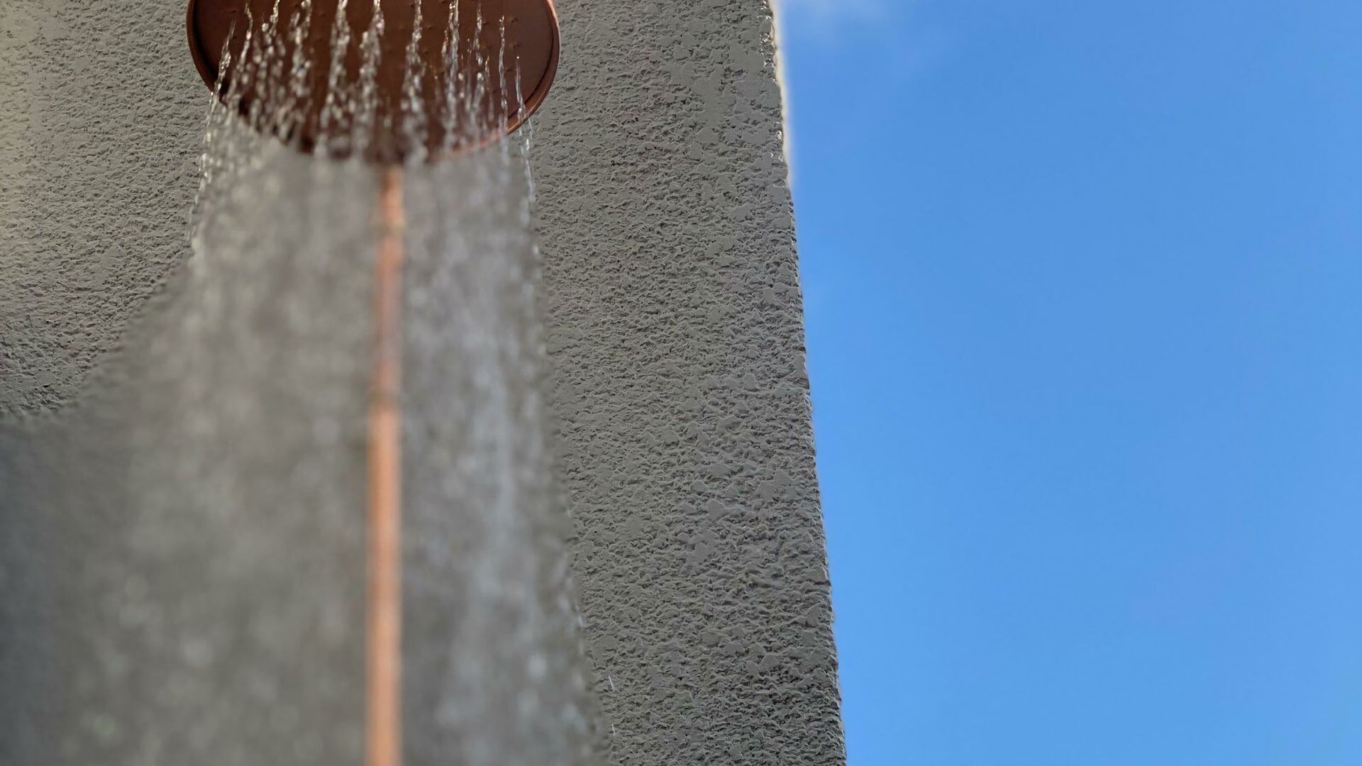 A close-up of a water spout with water flowing down a textured wall.