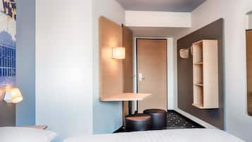 Ein modernes Hotelzimmer mit Bett, Nachttischen, einem Wandregal, einer Tür und einem kleinen Hocker.