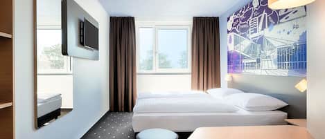 A hotel room with a bed, a TV, a desk, and a window with curtains.