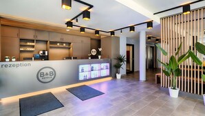 Un espace d’accueil moderne, comprenant un comptoir de réception, un écran numérique et des plantes en pot.