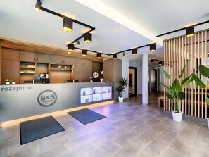 Un espace d’accueil moderne, comprenant un comptoir de réception, un écran numérique et des plantes en pot.