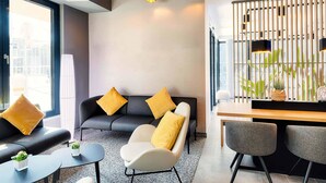 Une chambre d’hôtel moderne équipée d’un canapé, de fauteuils, d’une petite table et d’un coin repas avec des chaises.