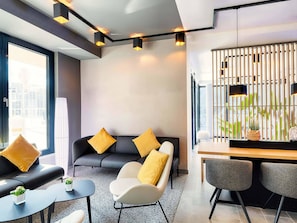 Une chambre d’hôtel moderne équipée d’un canapé, de fauteuils, d’une petite table et d’un coin repas avec des chaises.