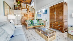 A spacious living room with a high ceiling, a wooden staircase, a large wooden cabinet, and a sofa with tropical cushions. - Roomy 2-Story w/Updated Kitchen–Kamaole Sands 4403 (KIHEI)