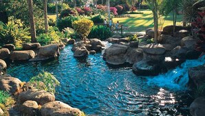 A serene garden with a small stream, large rocks, and palm trees. - Roomy 2-Story w/Updated Kitchen–Kamaole Sands 4403 (KIHEI)