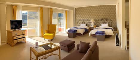 A hotel room with two beds, a sofa, a TV, and a balcony with yellow curtains.