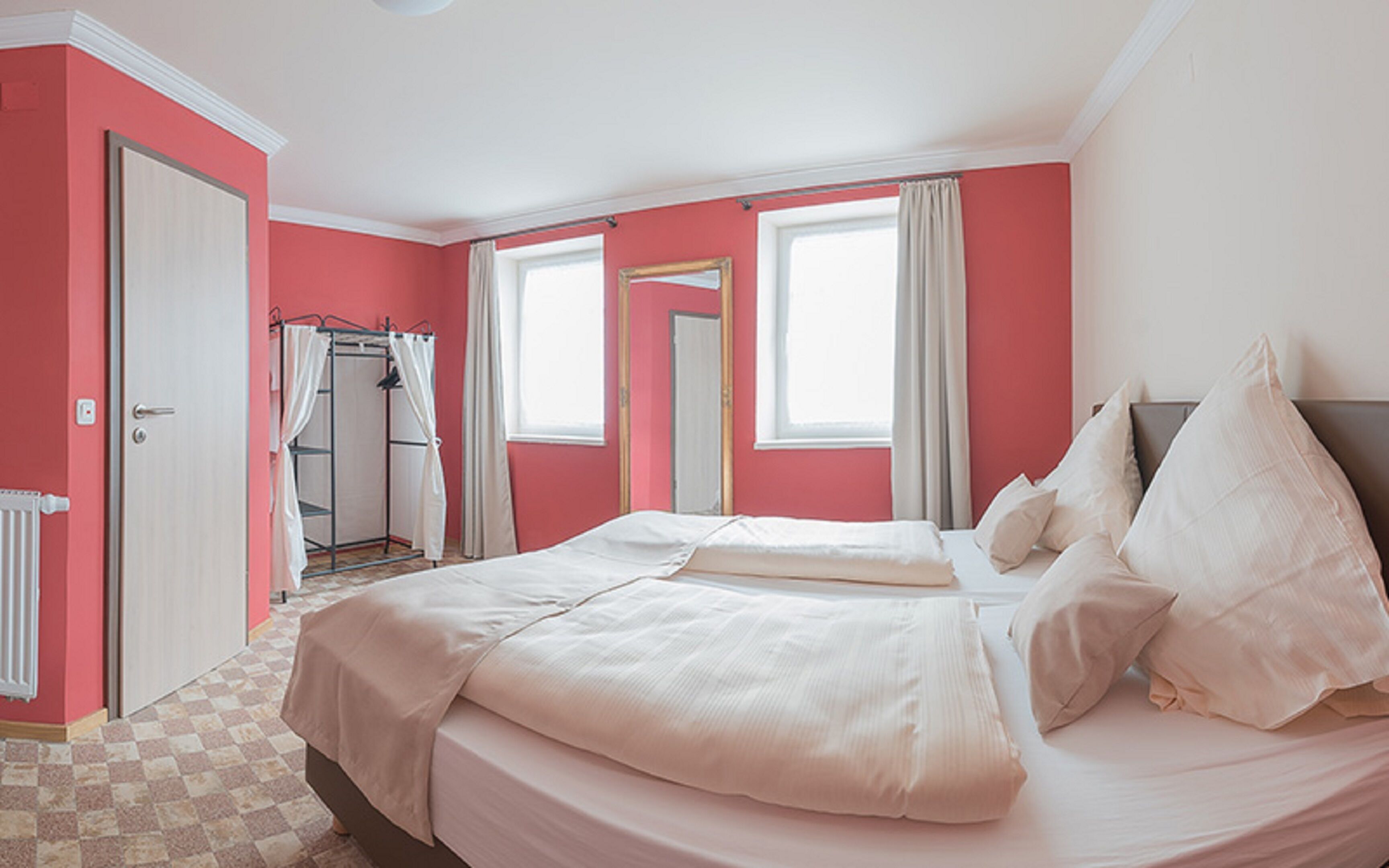 A hotel room with a large bed, a wardrobe, a mirror, and a window with curtains.
