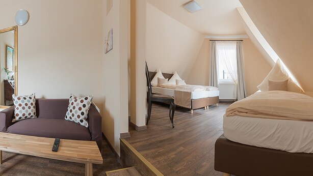 A modern hotel room with a wooden floor, a sofa, a bed, and a desk. - 7 Zwerge Übernachtungspension (Lohr am Main)
