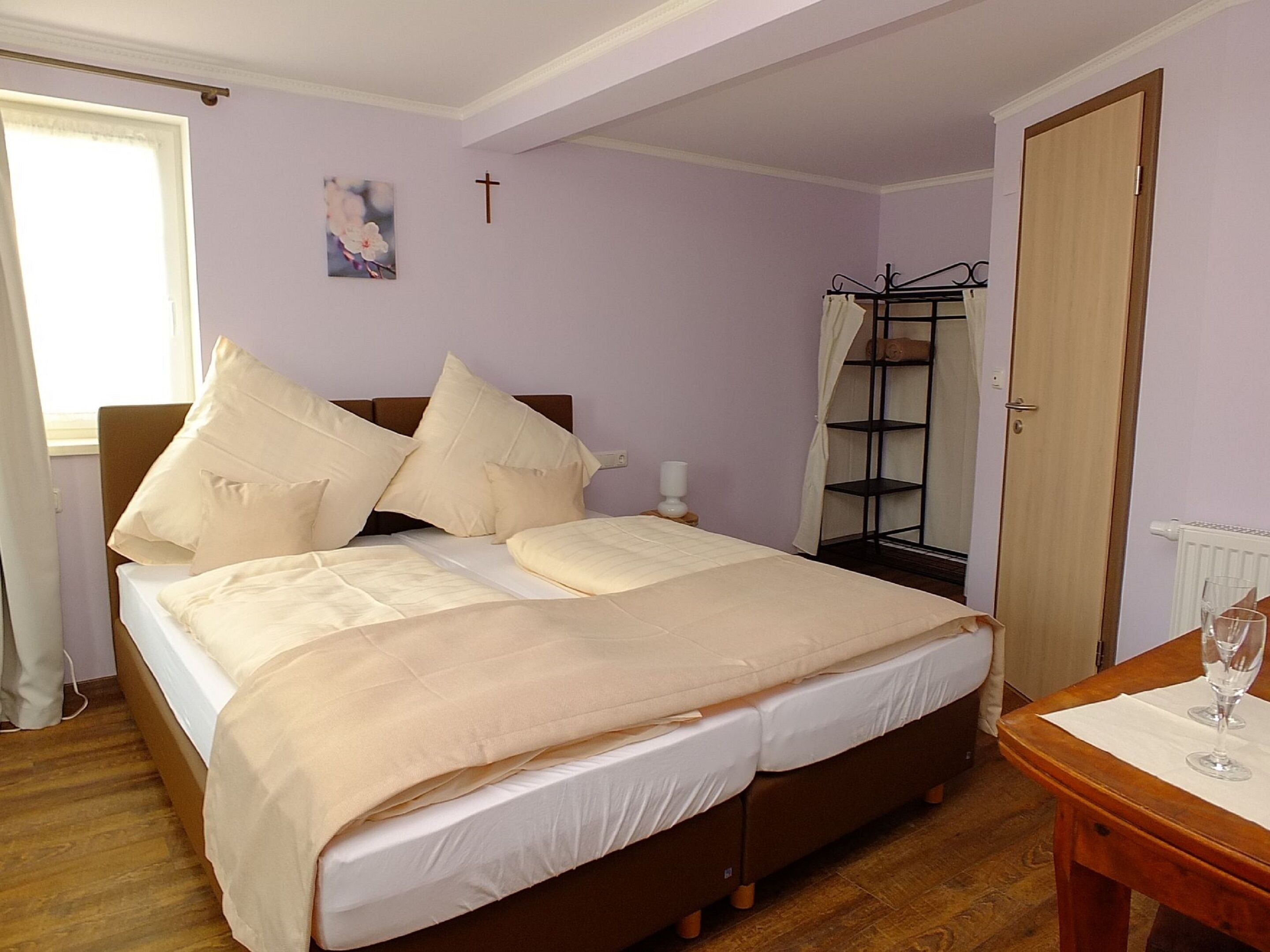 Une chambre à coucher avec un lit, une table de chevet, une fenêtre, une croix au mur et une porte.