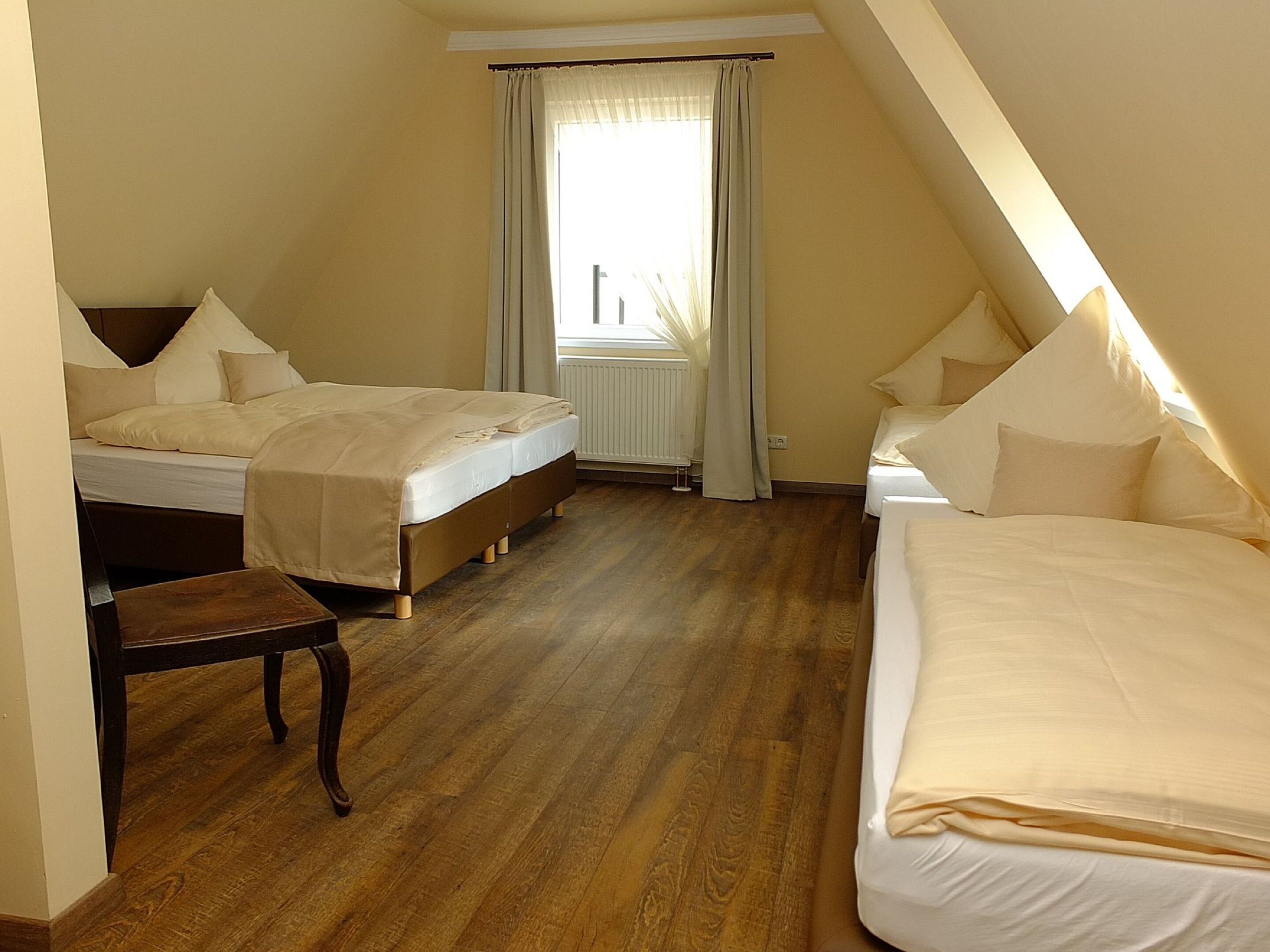 Ein Schlafzimmer mit zwei Betten, Holzboden, Heizkörper und einem Fenster mit Vorhängen.