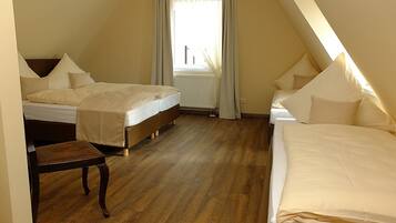 Ein Schlafzimmer mit zwei Betten, Holzboden, Heizkörper und einem Fenster mit Vorhängen.