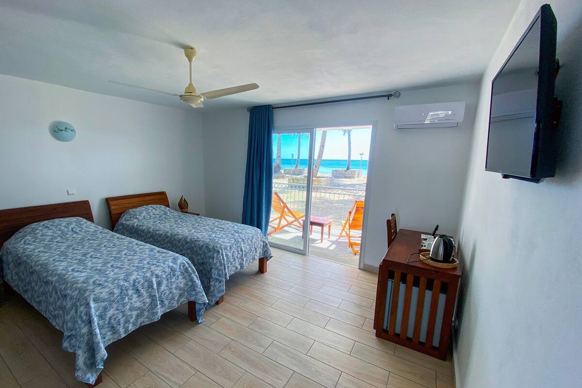 Ein Zimmer mit zwei Betten, einem Deckenventilator, einem Fernseher und Meerblick.