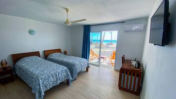 A room with two beds, a ceiling fan, a TV, and a view of the beach.