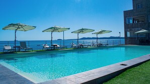 A swimming pool with lounge chairs and umbrellas, a clear view of the sea, and a building with balconies. - Orangea Beach Resort (Nosy Be)