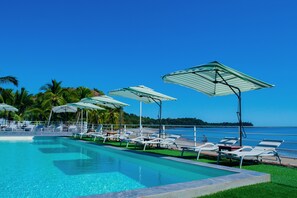 A poolside area with lounge chairs and umbrellas, a clear blue sky, and a view of the sea. - Orangea Beach Resort (Nosy Be)