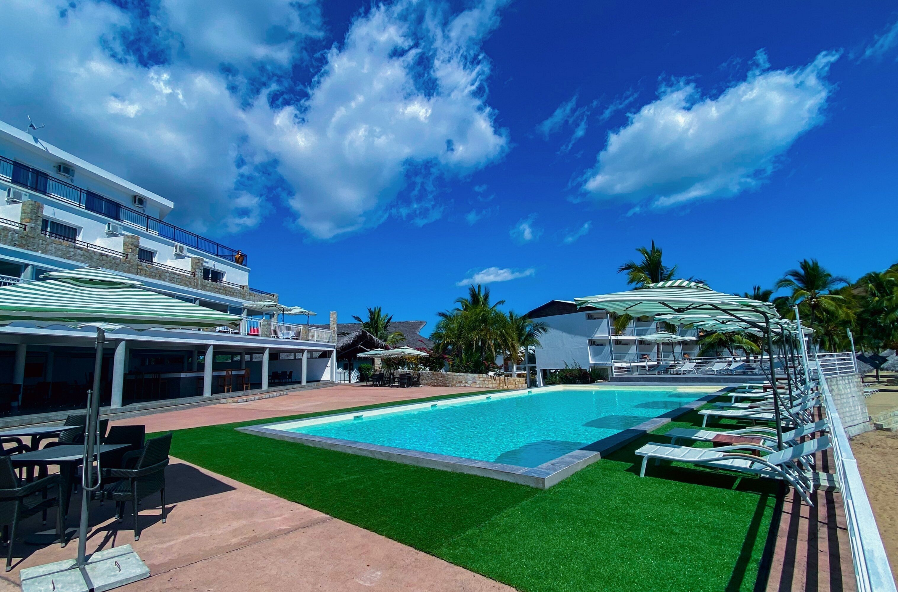 A pool area with artificial grass, lounge chairs, and a building with a balcony.