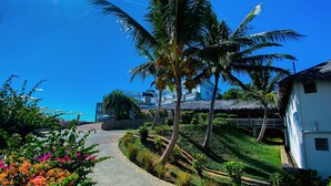 A pathway leading to a building with a thatched roof, surrounded by palm trees and flowering plants. - Orangea Beach Resort (Nosy Be)