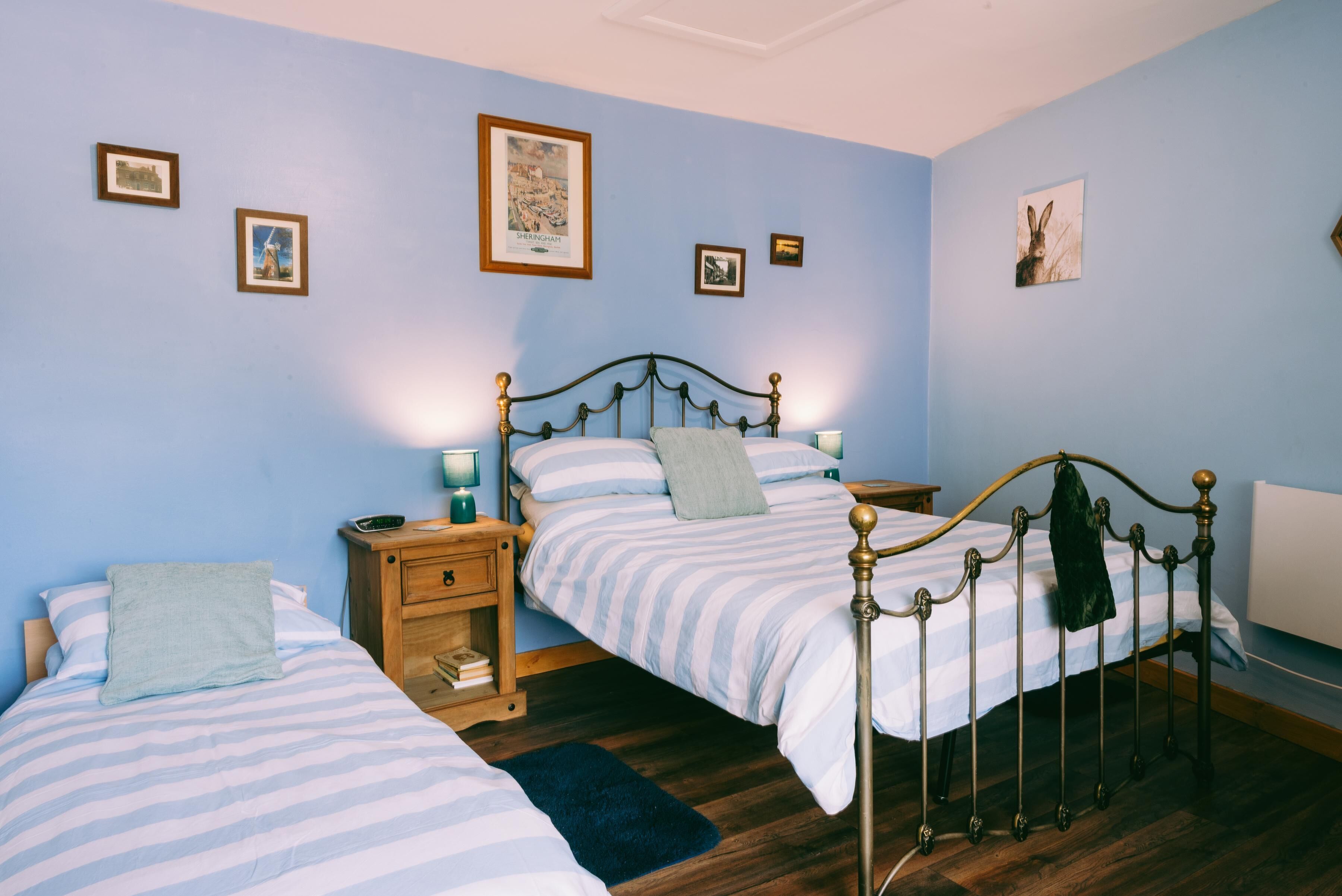 A bedroom with two single beds, wooden nightstands, and a blue wall with framed pictures.