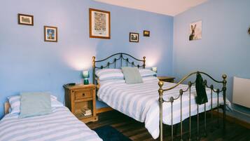 A bedroom with two single beds, wooden nightstands, and a blue wall with framed pictures.