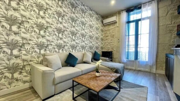 Ein Wohnzimmer mit ornamentalem Wandpapier, einer Couch, einem Couchtisch und einem Fenster mit Vorhängen.