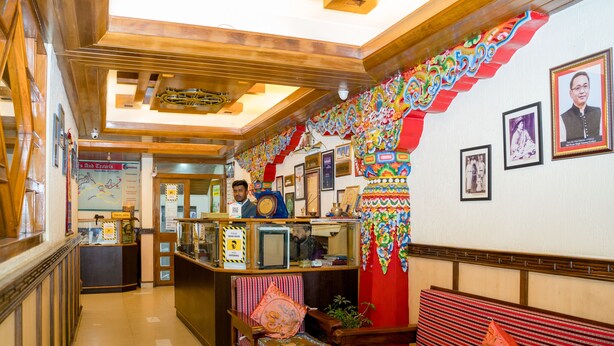 A reception area with a counter, a wooden bench, and a wall decorated with colorful patterns and framed pictures. - Doma Residency (Gangtok)