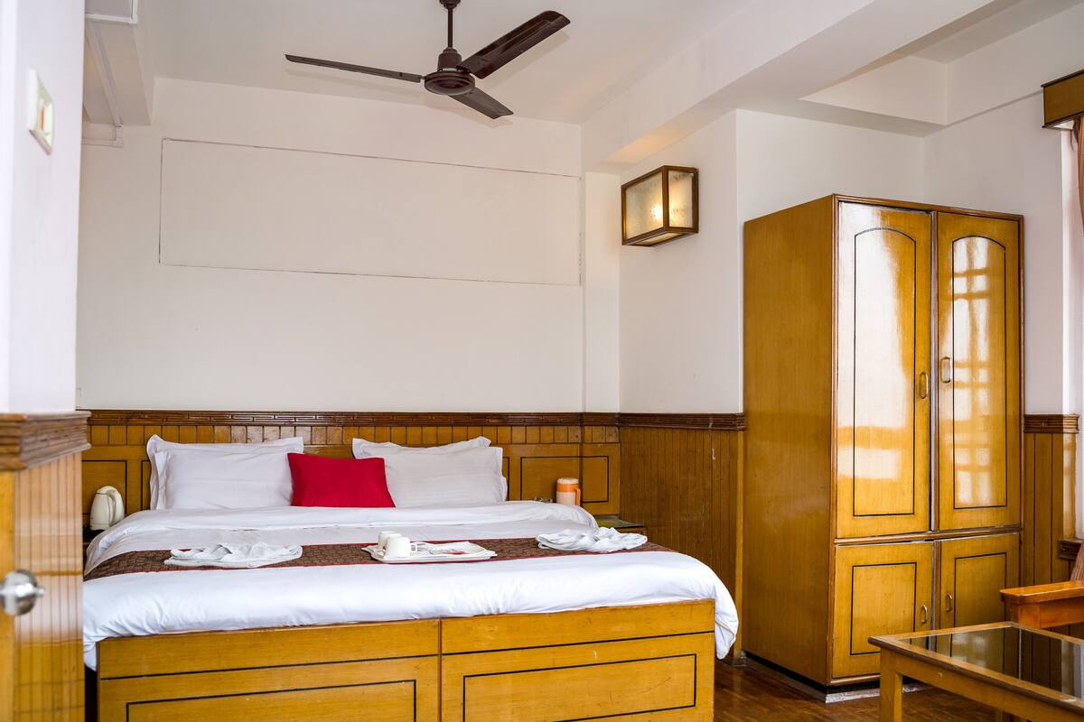 Una habitación de hotel con cama de madera, ventilador de techo, armario y mesita de noche.