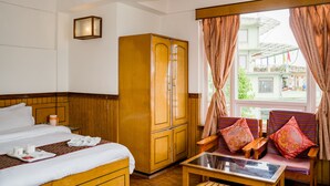 A hotel room with a bed, a wardrobe, a sofa with cushions, a table, and a window with curtains. - Doma Residency (Gangtok)