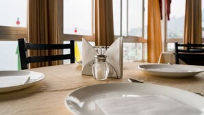 A dining table with white plates, a salt shaker, and a napkin holder. - Doma Residency (Gangtok)